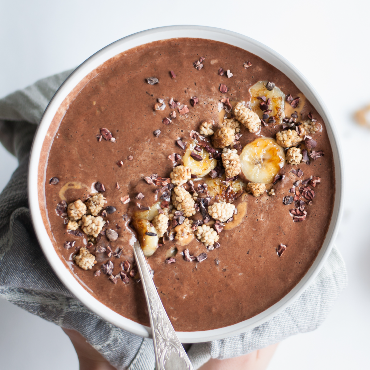 Chocolate smoothie bowl with mulberries, banana slices and cacao nibs in a white bowl.
