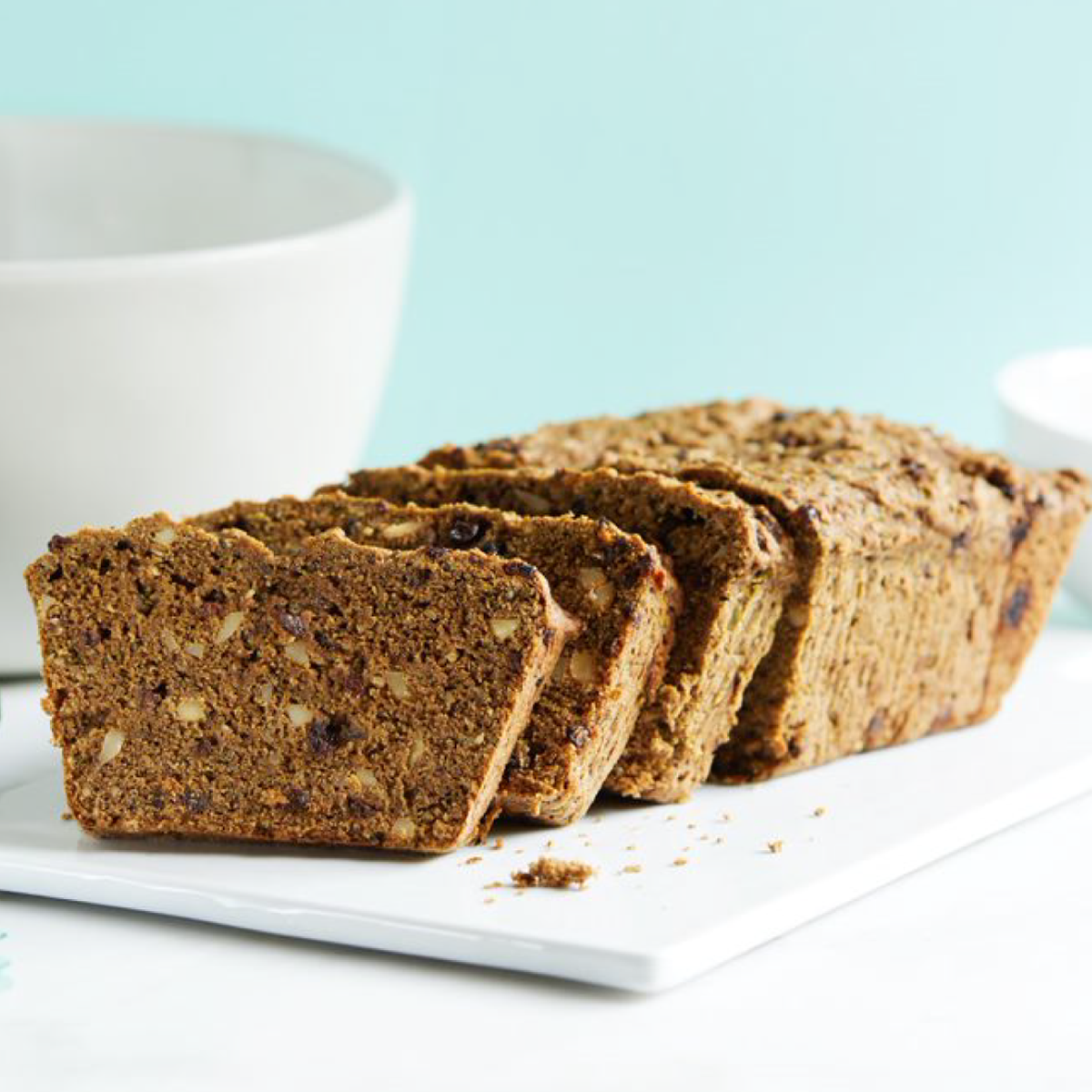 Loaf of banana bread with slices on a white plate against a light blue background