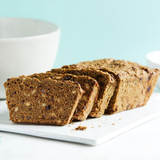 Loaf of banana bread with slices on a white plate against a light blue background