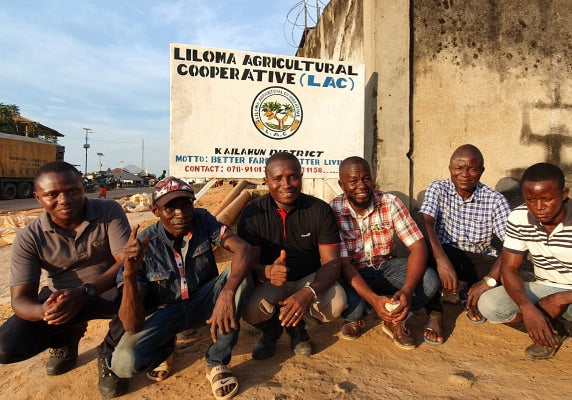 Farmers sitting together by the Lilona Agricultural Cooperative sign