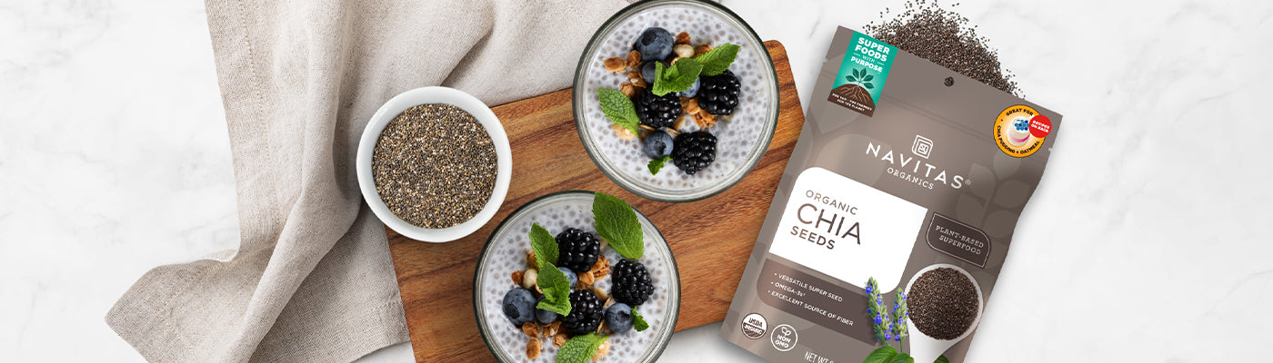 Two dishes filled with chia pudding topped with berries, nuts and mint leaves next to a dish filled with chia seeds and a spilling bag of Navitas Organics Chia Seeds.