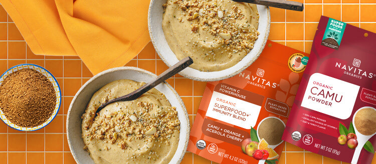 An orange countertop with two smoothie bowls, a dish filled with organic camu powder and bags of Navitas Organics Superfood+ Immunity Blend and Camu Powder.