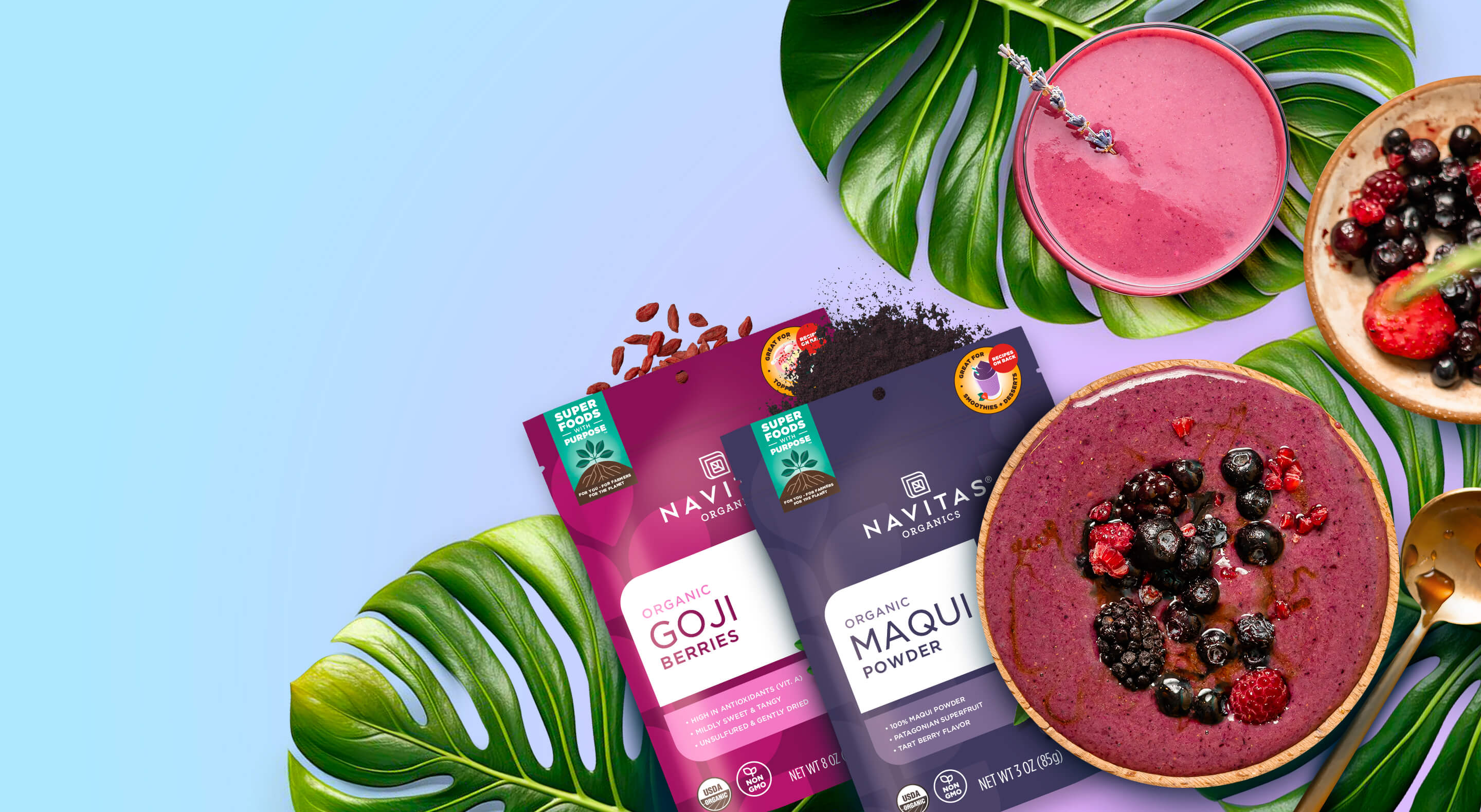 Bags of Navitas Organics Goji Berries and Maqui Powder spilling out product next to smoothies, palm leaves and a gold spoon against a colorful background.