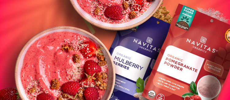 Two bowls of vibrant pink smoothies topped with seeds and strawberries, adjacent to packages of Navitas Organics Mulberry Berries and Pomegranate Powder.