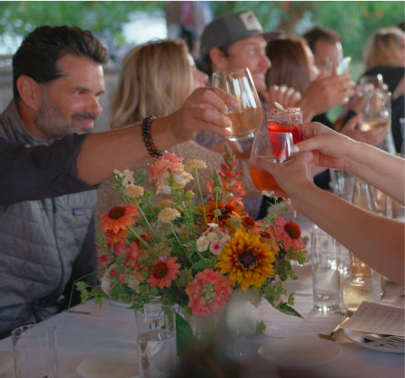 Navitas group making a toast together around a long table with flowers and glasses.