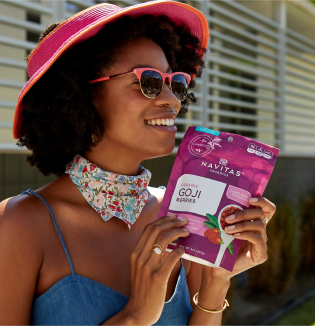 A woman in sunglasses and hat holding a bag of Navitas Organics Goji berries