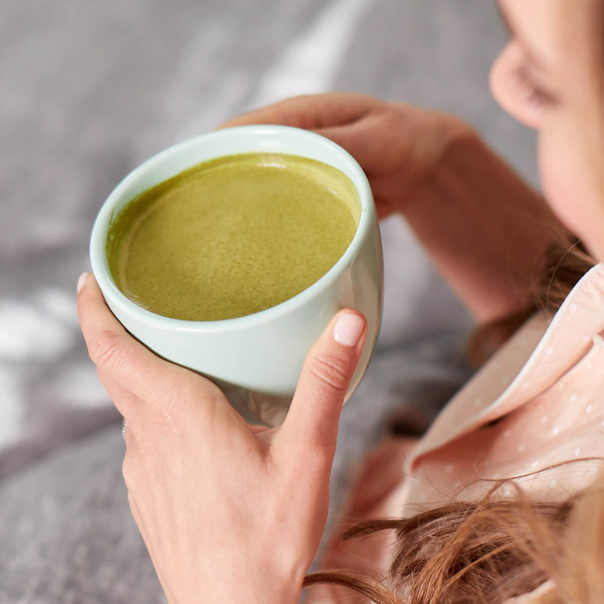 A woman sipping on a mug filled with a prepared Navitas Organics Matcha Latte