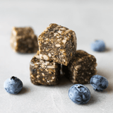 Navitas Power Snack Blueberry Hemp snack bites with blueberries alongside on a white counter.