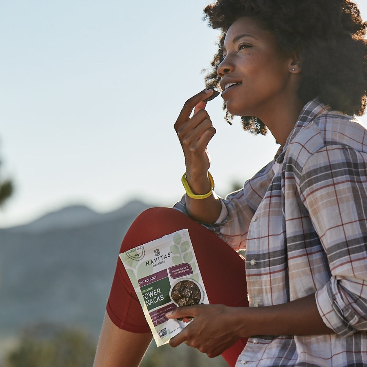 Woman enjoying Navitas Power Snacks Cacao Goji outside with mountains in the background.