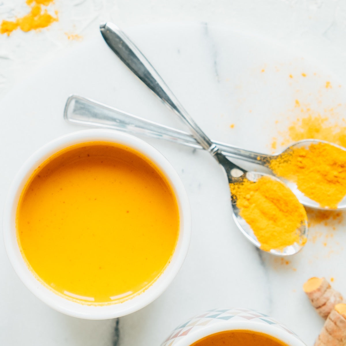 Navitas Turmeric Powder in spoons on a counter with a turmeric sauce in a bowl.
