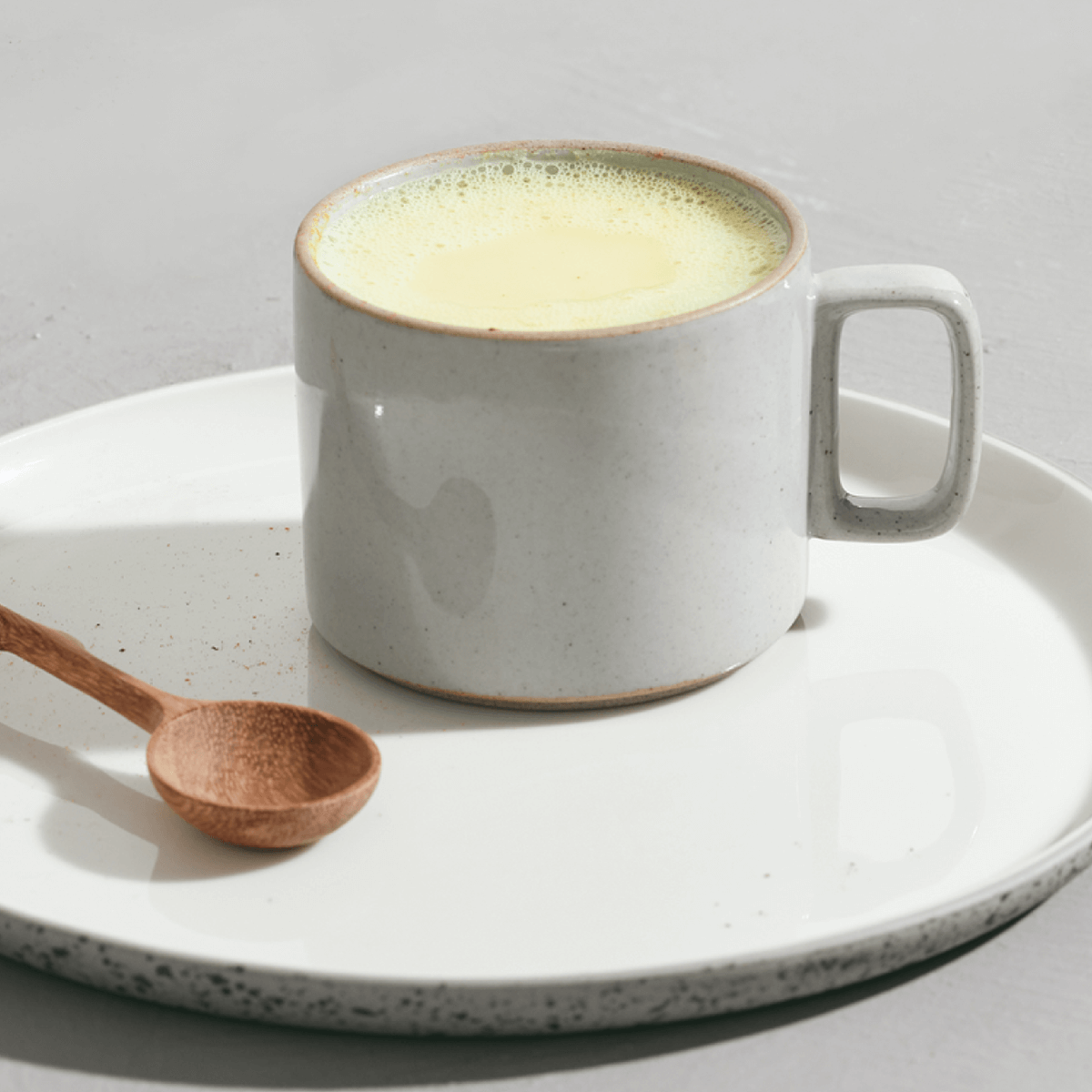 Frothy hot drink in a mug with a spoon alongside.
